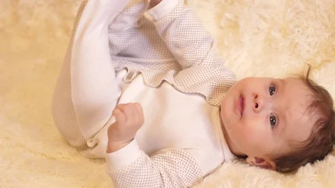 Infant lying on his back, playing with his feet and smiling. Slow motion. Stock Footage 81095861