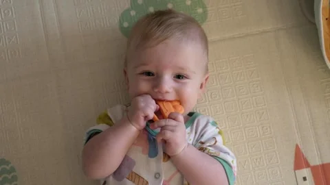 Infant lying on play mat chews colorful teether designed for teething relief Stock Footage 316038390