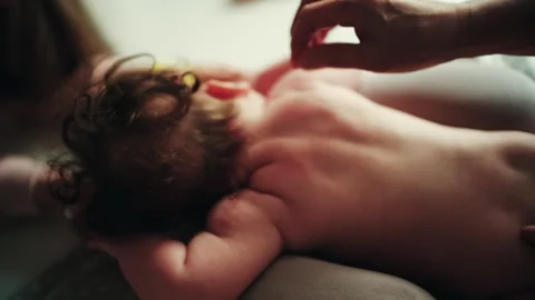Infant lying on stomach while caregiver gently massages baby's back during 스톡 동영상 331057941