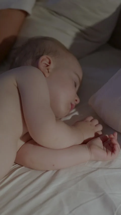 Infant peacefully sleeping on a bed with soft white sheets, a pillow nearby, and Stock Footage 341898768