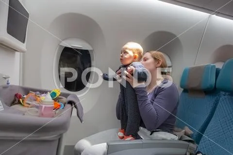 Infant plays on mother hands at the airplane. Amazed of tablet monitor and f Stock Photos