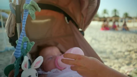 Infant receiving bottle feeding in a stroller on a sandy beach, enjoying summer Stock Footage 343227890