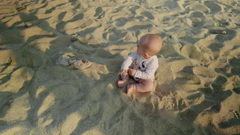 Infant sitting on sandy beach, exploring surroundings with curiosity, sunlight Video stock 317329643