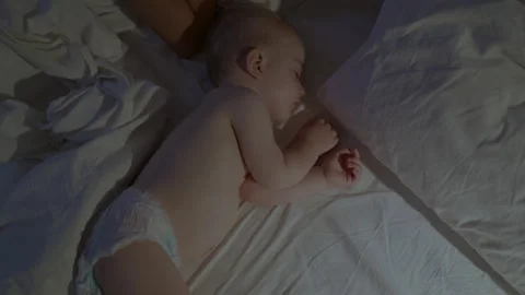 Infant sleeping peacefully on a bed with white sheets, soft light illuminating Stock Footage 341524064