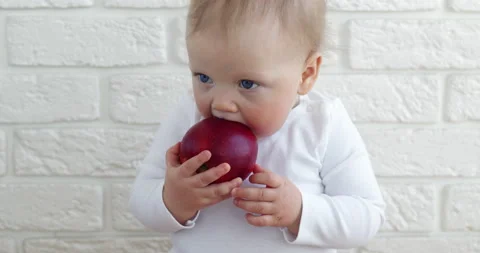 Infant tries to bite fresh apple sitting against brick wall 스톡 동영상 187613793