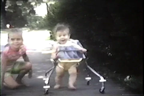 Infant in walker with sister on sidewalk, 1968 Video stock 36089936