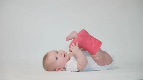 An infant on a white background lies on its back wearing a pink boot Video stock 237242635