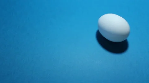 Infinitely rotating white chicken egg on blue background Video stock 231140793
