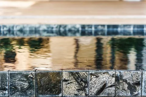 Infinity pool edge with dark stone tiles and water reflection Stock Photos