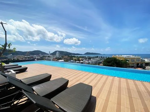 Infinity pool with lounge chairs overlooking cityscape and ocean under blue sky Фото
