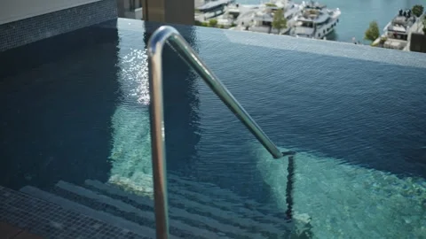 Infinity pool with mosaic steps and handrail by marina with yachts Stock Footage 329412202