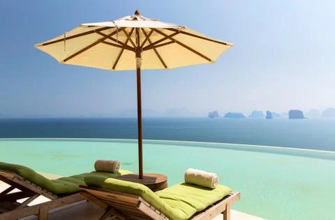 Infinity pool with parasol and sun beds at ocean Stock Photos