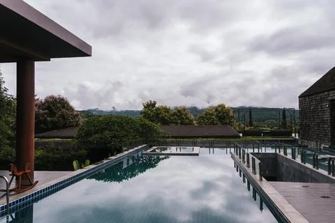 Infinity pool reflecting a cloudy sky above green hills in Pai, Thailand Foto stock