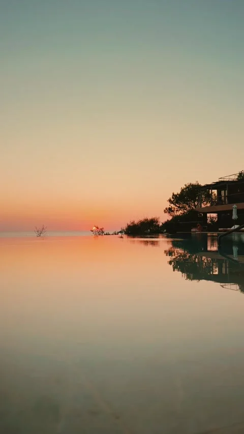 Infinity Pool Reflecting Sunset Sky with Calm Water and Poolside Trees Stock Footage 341527348