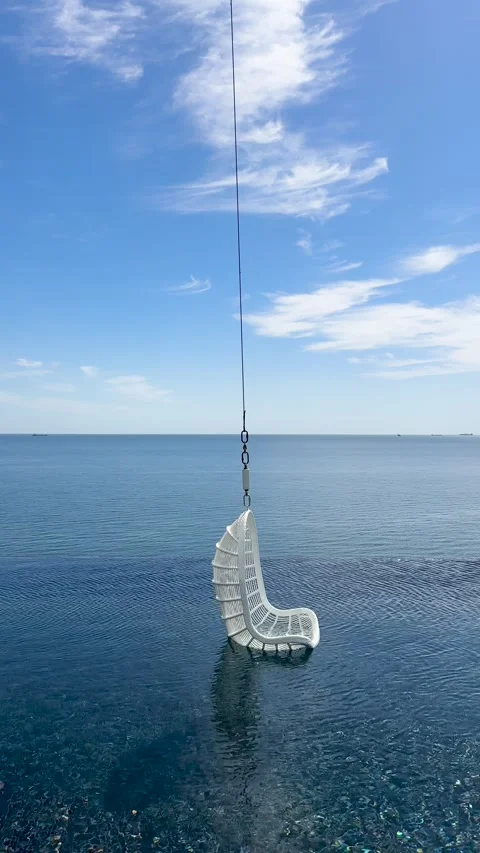 Infinity pool with a white hanging wicker chair swaying over moving blue water Video stock 335828663