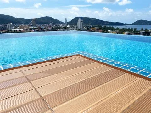 Infinity pool with wooden deck overlooking cityscape and mountains under a clear Stock Photos