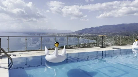 Infinity swimming pool with inflatable swan toys on the water Stock Footage 160784652