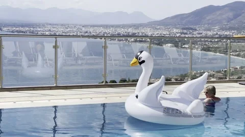 Infinity swimming pool with inflatable swan toys on the water Stock Footage 160784907