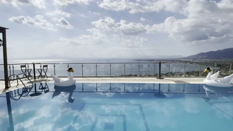 Infinity swimming pool with inflatable swan toys on the water Stock Footage 160785059
