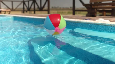 An inflatable ball floats on a blue pool with clear water under the summer sun Stock Footage 348086099