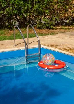 Inflatable ball resting inside red lifebuoy floating in clear blue pool. Conc Stock Photos