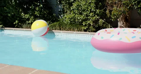 Inflatable beach ball and donut float drifting across sunlit backyard pool under Stock Footage 310360582