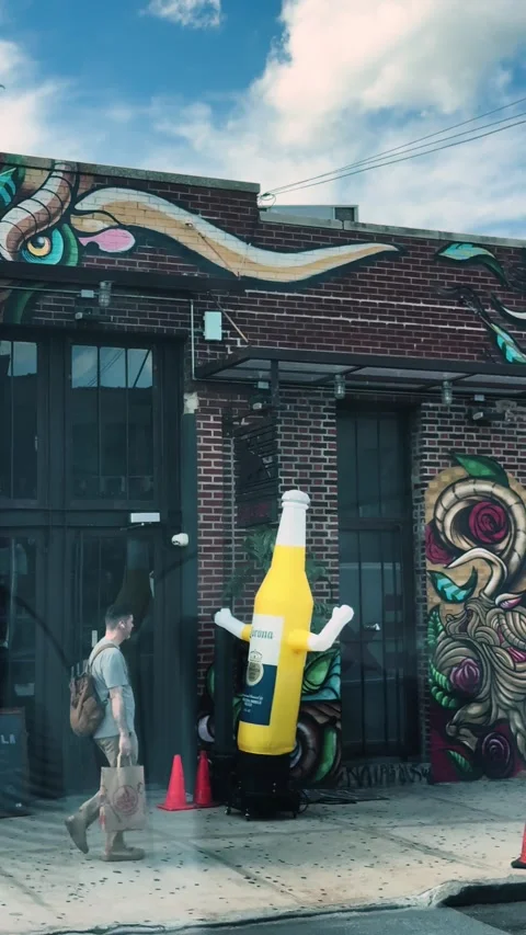 Inflatable Bottle Figure Waving Outside Colorful Mural Building in Brooklyn Stock Footage 337910080