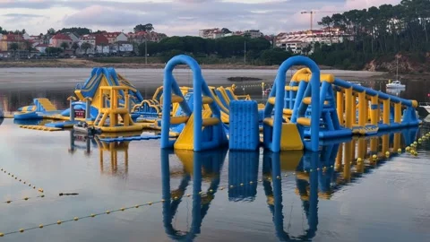Inflatable Floating Water Park on Calm Sea Beside a Coastal Town at Dusk Stock Footage 341434098
