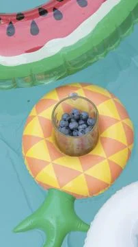 Inflatable pineapple and blueberries in pool. Healthy eating and vacationing in Stock Photos