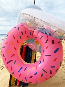 Inflatable pink donut-shaped pool float with colorful sprinkles resting on sandy Stock Photos