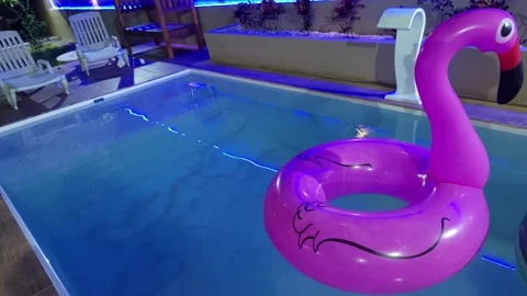 Inflatable pink flamingo float in a blue-lit swimming pool at night. 스톡 동영상 312898160