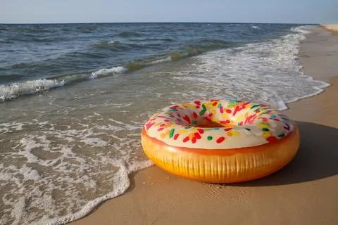 Inflatable ring with doughnut pattern on sandy beach near sea, space for text Stock Photos