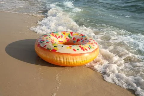 Inflatable ring with doughnut pattern on sandy beach near sea Stock Photos