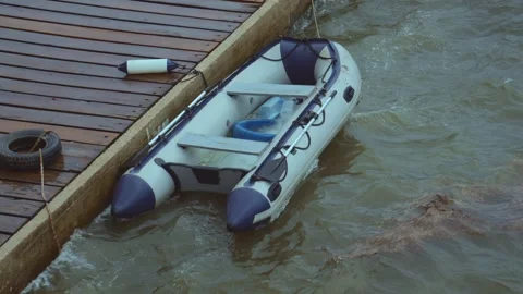 An inflatable rubber boat has been driven by a storm to the pier rocking on Stock Footage 313731446