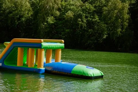 Inflatable water park obstacle course on a lake amidst lush greenery. Weekend Stock Photos