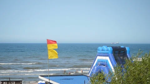 Inflatable Water slide on the Sandy beach in Europe. Baywatch red yellow Flag. Stock Footage 129381466