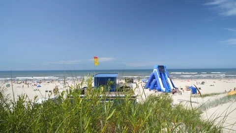 Inflatable Water slide on the Sandy beach in Europe. Baywatch red yellow Flag.  Stock Footage 129383553