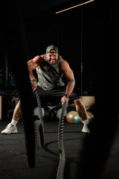 Inflated man tensely performs an exercise with ropes Stock Photos