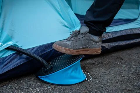 Inflating blue tent using a foot pump and grey sneakers in the outdoors. Stock Photos
