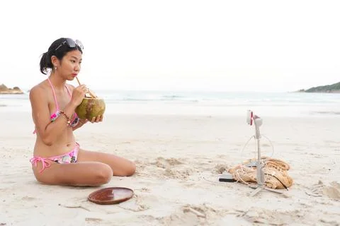 Influencer drinking a coconut juice while doing a live using a mobile on the Stock Photos