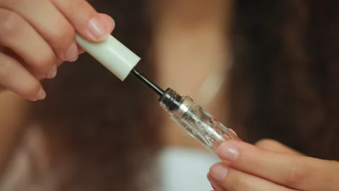Influencer prepares makeup using wand and bottle on vanity table. Person with Stock Footage 345136911