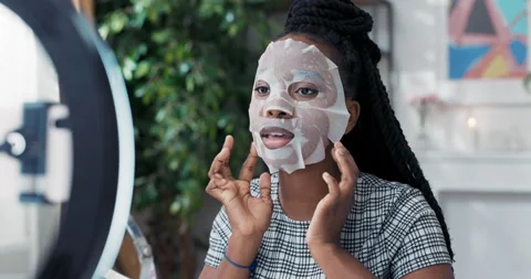 Influencer records beauty tutorial applies sheet mask to face uses ring light 動画素材 179946065