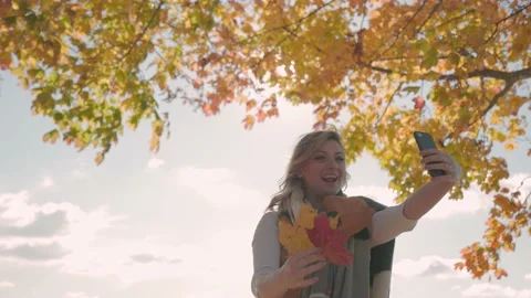 Influencer vlogging on smartphone with fall leaves in the background, content Stock Footage 220598271