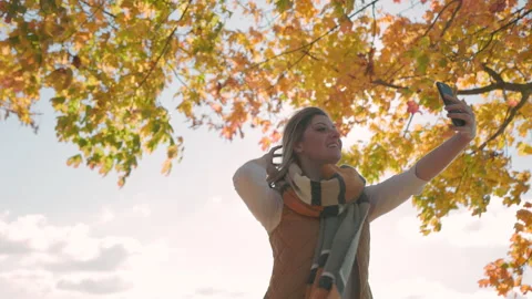 Influencer vlogging on smartphone with fall leaves in the background, content Stock Footage 220598879
