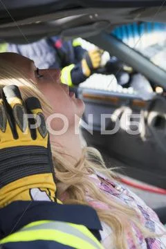 Injured woman in car with firefighter in background cutting out windshield Stock Photos