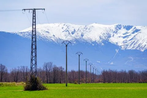 Inline power poles that move away towards the high snow-capped mountains in the Stock Photos
