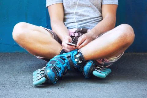 Inline roller skater with phone sitting against blue wall. Stock Photos