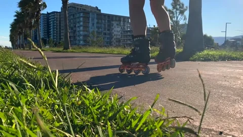 Inline skater rolling past camera, ground-level side view on a paved path Stock Footage 345361773