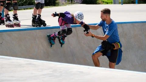 Inline skating coach helping young girl practice bowl drop Stock Photos