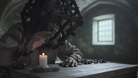 Inmate in head cage looking at a burning candle and warming his chained hand Stock Footage 340322647
